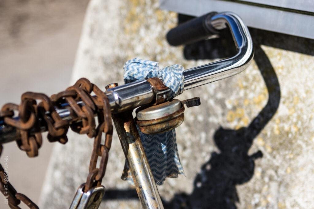 Ein alter Fahrradlenker mit rostiger Klingel und einem verrosteten Schloss, das am Lenker hängt.